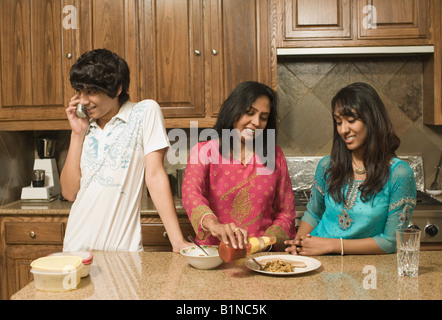 Teenager reden über ein schnurloses Telefon und seine Mutter und Schwester Ketchup auf eine Platte gießen Stockfoto