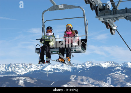 Kleinen Kindern Skifahrer reiten bis Sessellift mit Bergspitzen in der backgroung Stockfoto