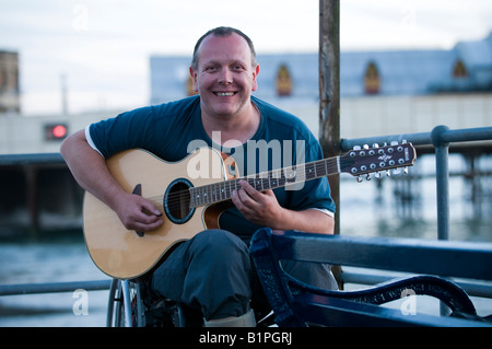 Lächelnd Mann sitzt im Rollstuhl, die Gitarre im Freien, Aberystwyth, Wales UK deaktiviert Stockfoto