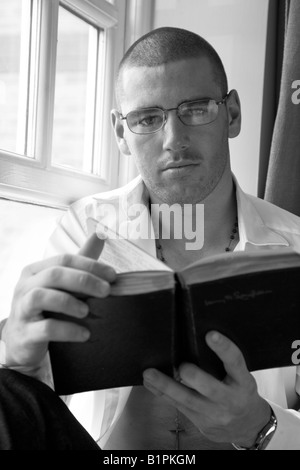 Gut aussehender junger Mann sitzt im Fenster ein Buch zu lesen Stockfoto