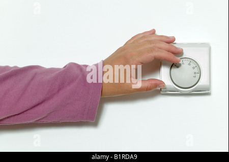 Womans Hand drehen Sie die Temperatur auf ein Raumthermostat Stockfoto