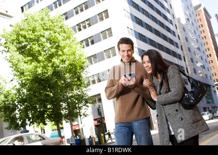 Ein junges Paar sind wandernde Arm in Arm durch eine Innenstadt mit einem Handgerät. Stockfoto