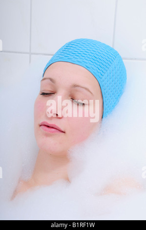 Hübsche junge Frau unter Bad in der Badewanne und entspannend, Badekappe blau Stockfoto