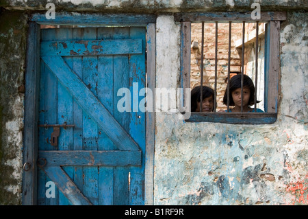 Zwei Mädchen auf der Suche durch ein vergittertes Fenster in den Slums von Pilkana, Howrath, Westbengalen, Indien Stockfoto