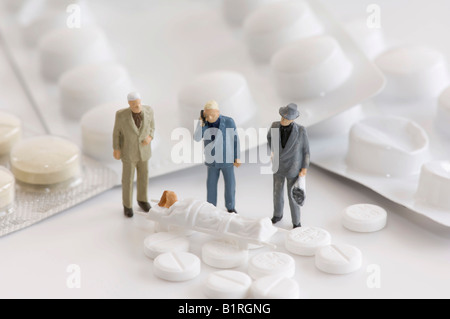 Tabletten, Blisterverpackungen und drei Miniatur-Männer stehen neben einer Frau auf einer Bahre, symbolische Foto Stockfoto