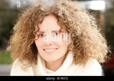 Frau mit lockigem Haar tragen einen weißen Pullover und lächelnd Stockfoto