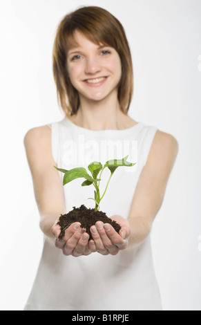 Junge Frau Schröpfen eine junge Pflanze verwurzelt im Boden in ihren Händen Stockfoto