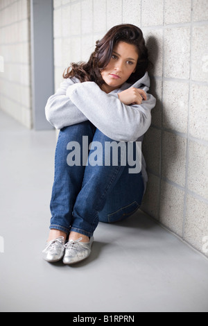 Junge Frau, die leider auf dem Boden an eine Wand gelehnt sitzend Stockfoto