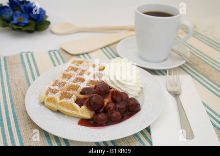 Waffel mit Puderzucker, Kirschen und Sahne serviert mit einer Tasse Kaffee gekrönt Stockfoto