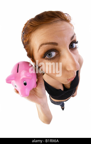 Frau hält ein Sparschwein zu ihrem Ohr, Fischaugen-Objektiv Stockfoto