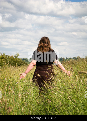 Frau allein zu Fuß unter langen Gräsern in einem Feld in East Yorkshire England UK Stockfoto