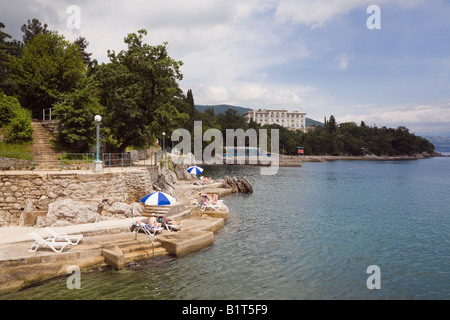 Lovran Istrien Kroatien Europa Menschen Sonnenbaden am Betonstrand unter Lungomare Promenade auf felsigen Küste der Kvarner Bucht Stockfoto