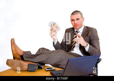 Junger Geschäftsmann mit Füßen auf seinem Schreibtisch und hält ein Bündel Geld. Stockfoto