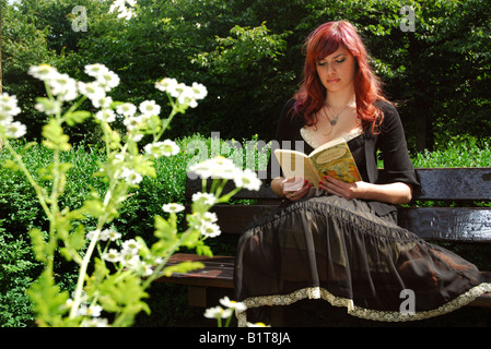 Märchen Mädchen Alice im Wunderland auf einer Parkbank sitzend lesen Stockfoto
