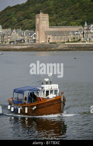 Stadt von Oban, Schottland. Kathedrale von St. Columba mit den lila Heidekraut Besuchern touring Boot in Oban Bay. Stockfoto