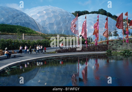 Eden Project.  Gesamtansicht über die feuchten Tropen Biom außen mit bunten Fahnen und Besucher zu Fuß am See. Stockfoto