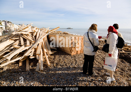 ENGLAND West Sussex Worthing drei Leute betrachten Holz Rückstand am Strand von Schiffbrüchigen Eisprinzessin mit entfernten Pier Stockfoto