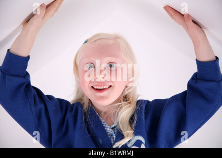 Kleine blonde behaarte Schulmädchen Strecken ihre Arme bis über den Kopf vor einem weißen Hintergrund Stockfoto