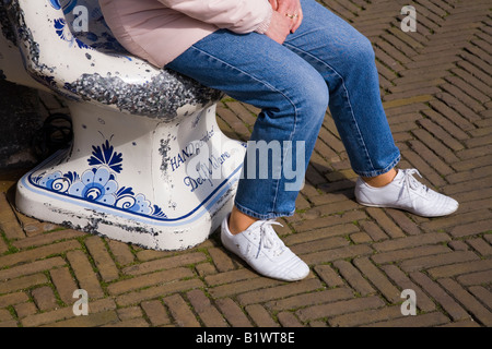 Eine Frau sitzen in einem großen keramischen übergroße Hand Platz draußen ein Geschäft für Royal Delfter Keramik, in Delft. Netherland Stockfoto