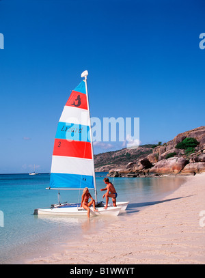 Zwei Personen bereiten ein kleines farbenfrohes Segelboot an einem ruhigen tropischen Strand mit klarem blauem Himmel vor Stockfoto