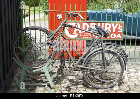 Altmodische Fahrräder in einem Fahrradständer auf dem erhaltenen Dampf Alter Bahnhof mit Werbung Emailleschild und rote Telefonzelle. Stockfoto