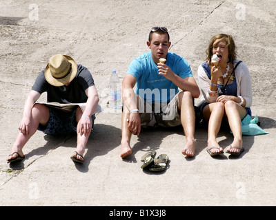 Drei junge Leute, zwei essen Eiscreme und eine Zeitung lesen Stockfoto