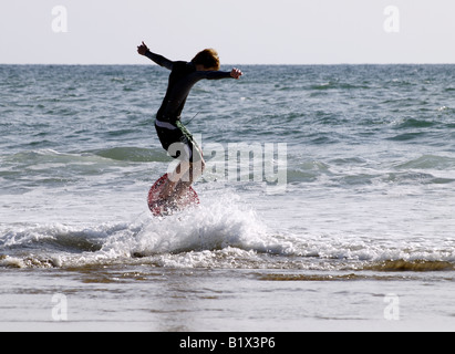 Teenager in ein Skimboard springen eine Welle Stockfoto