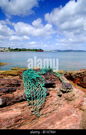 Die felsige Küste Goodrington im Süden in der Nähe von Paignton in Devon Blick nach Norden an einem Sommertag mit einem alten Fischernetz angespült Stockfoto