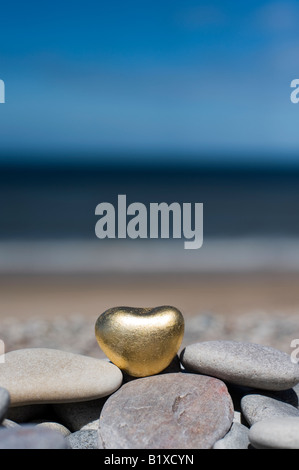 Goldenes Herz geformte Kiesel auf die Kieselsteine am Strand von Findhorn, Schottland Stockfoto