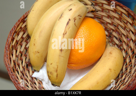 Bananen und eine Orange in einem Rohr-Korb Stockfoto