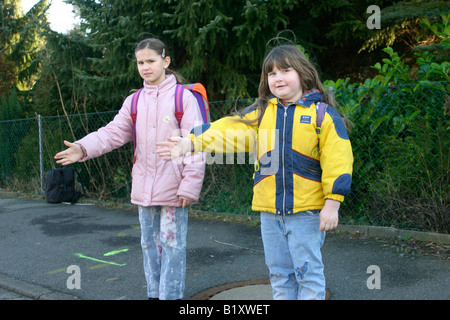 zwei junge Mädchen streckte ihre Arme um die Straße an einem Fußgängerüberweg überqueren Stockfoto