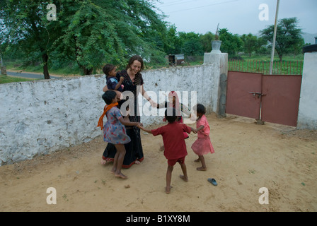 Eine junge westliche Frau spielt mit lokalen Dorfkinder im Hof eines Hauses aus Rajasthan, Thar-Wüste Rajasthan, Indien. Stockfoto