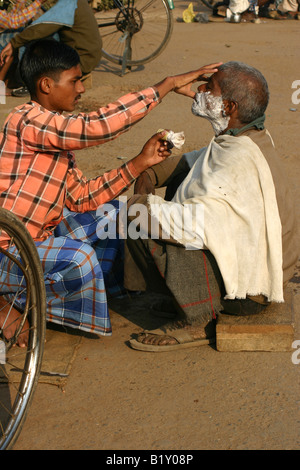 Barbier rasieren ein Kunde in den Straßen von Varanasi, Indien Stockfoto