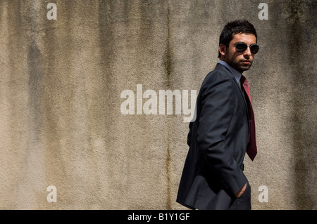 Business-Mann trägt Anzug und Sonnenbrille walking im freien Hände in den Taschen-Seitenansicht Stockfoto