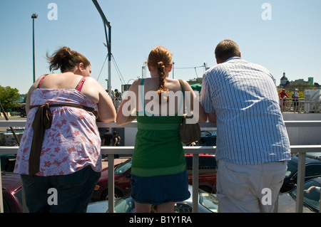 Drei Passagiere lean über ein Geländer, die Autos und Lastwagen auf dem Deck unten zu beobachten. Stockfoto