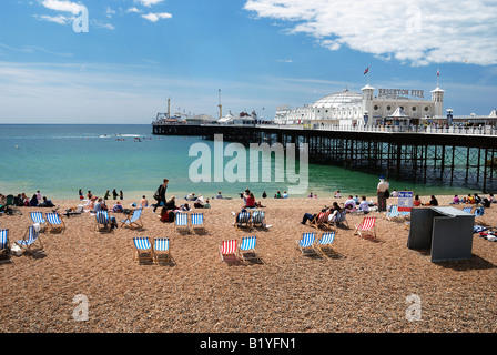 Touristen genießen die Sonne am Strand von Brighton mit Pier im Hintergrund Stockfoto