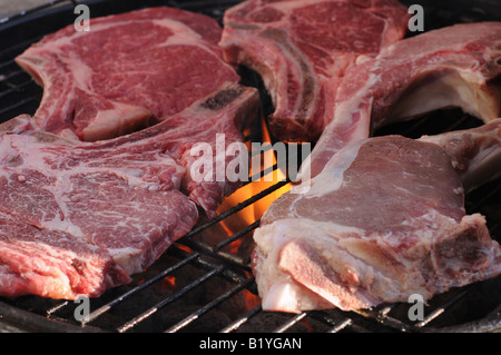 Steak und Kalbfleisch Koteletts brutzeln auf dem Grill Holzkohle Grill. Eine sanfte Flamme leckt an der Unterseite des Fleisches. Stockfoto