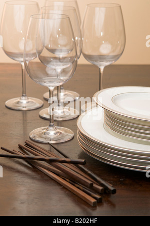 Ein Stapel von Weißware Gerichte sitzen auf einem Holztisch mit Weingläsern und hölzerne Stäbchen Stockfoto