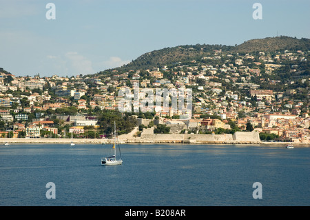 Ein Segelboot nähert sich die imposante Zitadelle vor Pastell farbigen Villen und Hotels von Villefranche Sur Mer Stockfoto