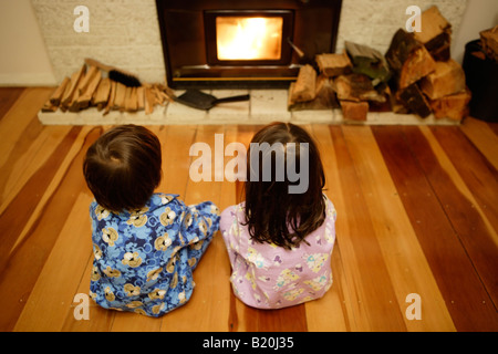 Jungen im Alter von sechs und Schwester im Alter von vier sitzt vor der Log brennendes Feuer Holz ist eine Null Kohlenstoff erneuerbarer Brennstoff Stockfoto