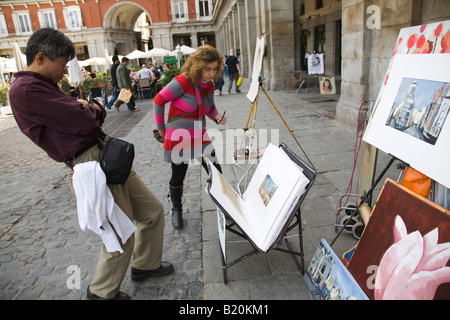 Spanien Madrid japanischen Mann studiert Malerei zum Verkauf im Plaza Mayor zurücklehnen und Prüfung Womans Kunst Stockfoto