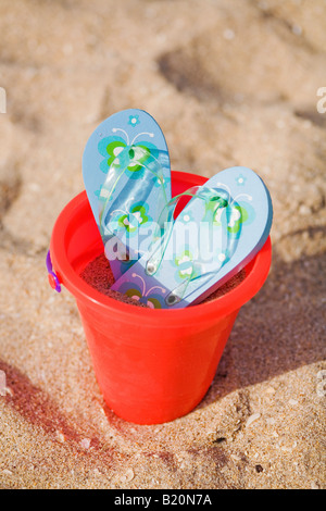 Paar blau Flip flops mit Blumen in einen Kunststoff Eimer am Strand gedreht. Stockfoto