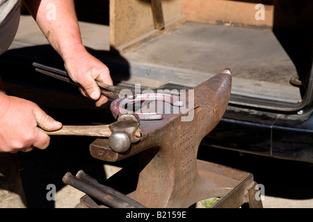 Ein Hufschmied arbeiten und gestalten eine rote heiße Hufeisen auf seinem Amboss. Stockfoto