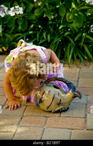 Ein zweijähriges Kind untersucht ein Fisch geformt Krug im Garten ihres Hauses im südlichen Kalifornien Hinweis orange Lutscher Stockfoto