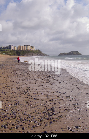 Eine Frau geht mit ihrem Hund zurück entlang der südlichen Strand in Richtung Tenby, Pembrokeshire, Wales, Großbritannien Stockfoto