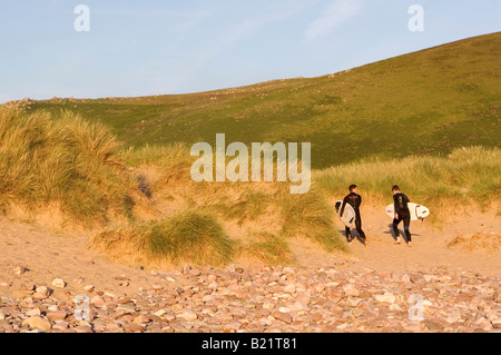 Surfer gehen über den grasbewachsenen Dünen hinter Llangennith Strand auf Rhossilli Bay, Gower Peninsula, South Wales. Stockfoto