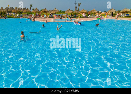 Horizontalen Weitwinkel ein belebtes Hotel Swimming Pool umgeben von vielen Rasen Sonnenschirme und Sonnenliegen Stockfoto