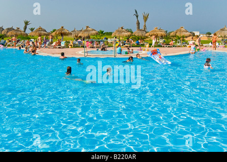 Horizontalen Weitwinkel ein belebtes Hotel Swimming Pool umgeben von vielen Rasen Sonnenschirme und Sonnenliegen Stockfoto