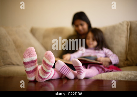 Indische Mutter der 30er Jahre und Mischlinge Tochter 4 lesen Sie ein Buch rosa gestreifte Socken Stockfoto