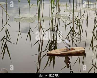 ein kleines Segelschiff auf See mit Seerosen und Schilf handgefertigt Stockfoto